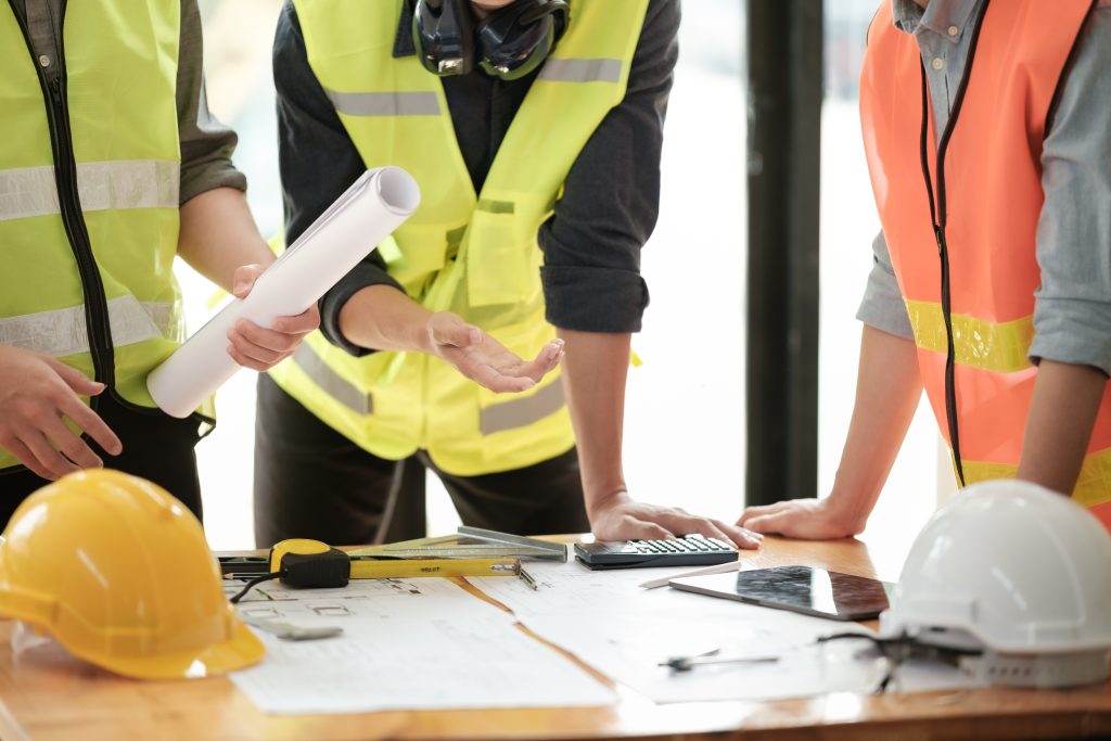 Architect reviewing detailed garden room blueprints and structural plans with a homeowner, discussing design elements and construction details at a modern workspace.